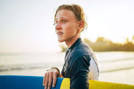 Portrait of a teen boy with Dental braces and wet hair with a surfboard goes for surfing. He is smiling and walking into the water. Happy boyhood and active vacation time concept.の写真素材
