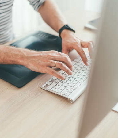 Writer typing modern computer keyboard writing novel sitting at the white wood table. Distance or freelance work on worldwide quarantine time conceptの写真素材