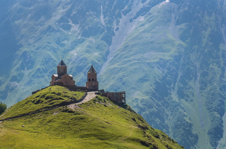 Gergeti Trinity Church XIV century on the green grass hill under Kazbek 5054m mountain. Landscape...