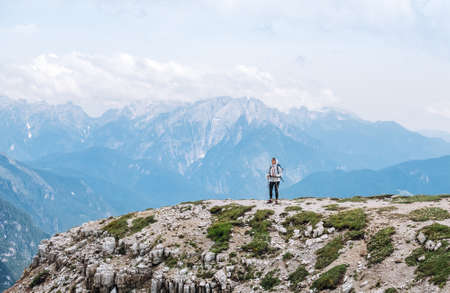 Woman trekker with backpack and trekking poles on the hill enjoying picturesque Dolomite Alps view near Tre Cime di Lavaredo formation in South Tyrol, Italy. Active people and mountain concept.の写真素材