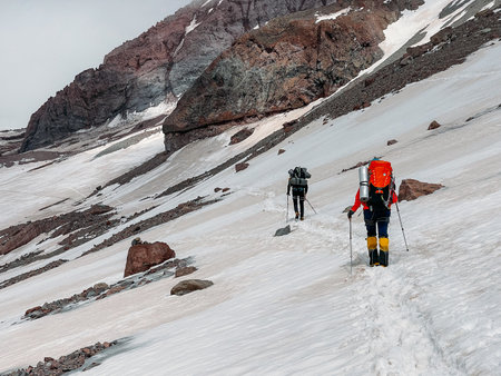Two mountaineers ascending Kazbek 5054m mountain with backpacks and trekking poles. Caucasus, Georgiaの写真素材