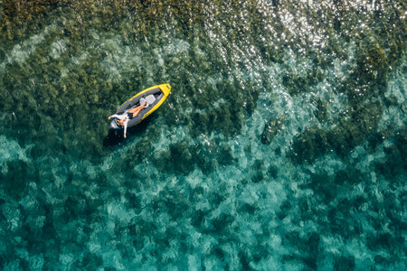 A lonely female in a straw hat smiling, relaxing lying floating in a kayak on the turquoise Adriatic Sea waves. Aerial coastal top view shot. Exotic countries vacations concept.の写真素材