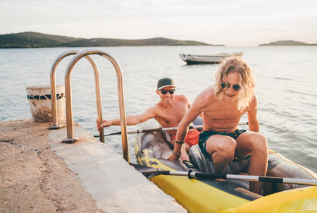 Father with teenager son on the bright yellow inflatable kayak returning back from evening ride by the Adriatic sea harbor in Croatia near from Sibenik city. Vacation and family values vertical image.の写真素材