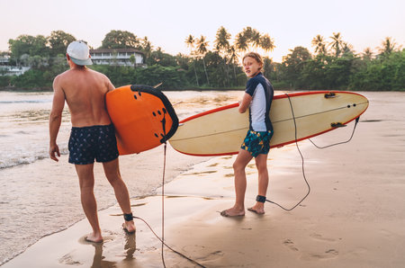 Teen boy with father with surfboards go to the sea for surfing on Sri Lanka island. They have a winter vacation and enjoying a beautiful sunset light Family active vacation conceptの写真素材
