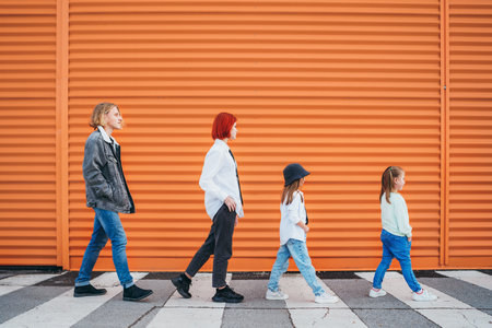 Fashion-dressed quartet of small kids and teenager sisters and brothers crossing a pedestrian zebra crosswalk on the orange wall background. Urban people living and street everyday life concept image.の写真素材