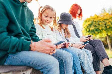 Little pretty girl portrait with sisters girls kids sitting in a row and browsing their smartphone devices. Careless young teenhood time and a modern technology concept image.の写真素材
