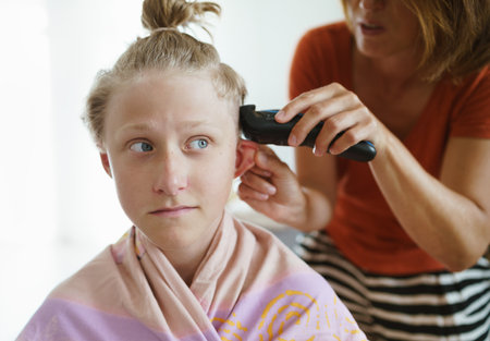 Mother trimming her son hairs making a modern hairstyle using electric electric trimmer at their home living room.の写真素材