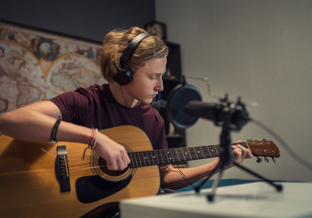 Microphone with pop filter closeup photo with a young teenager boy in headphones recording voice and guitar playing music. Modern home sound studio audio recording technology and teens hobby concept.の写真素材
