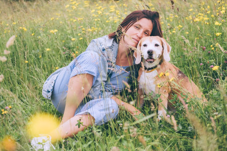 Beagle dog portrait with its woman owner looking at camera while sitting in high green grass. Female hugging her pet friend and looks slightly sad. Time spent with Cute pet family members  concept.の写真素材