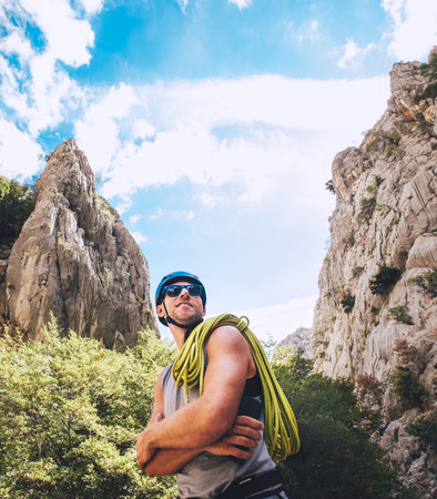 Portrait of smiling climber man in protective helmet and sunglasses with climbing rope on the shoulder standing in Paklenica park between rock cliff walls. Active extreme sports time spending concept.の写真素材