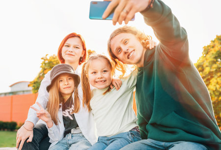 Portraits of three smiling sisters and brother teen taking selfie portrait using a modern smartphone camera. Careless young teenhood and childhood time and modern technology concept image.の写真素材