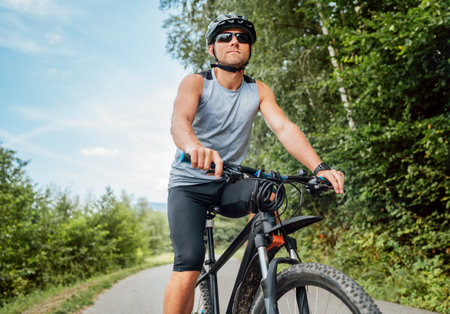 Portrait of happy man dressed in cycling clothes, helmet and sunglasses riding a bicycle on the out-of-town bicycle path. Active sporty people concept image.の写真素材