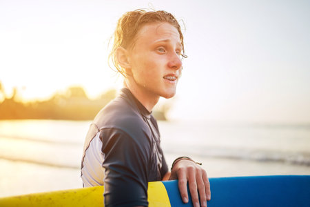 Portrait of a teen boy with Dental braces and wet hair with a surfboard goes for surfing. He is smiling and walking into the water. Happy boyhood and active vacation time conceptの写真素材