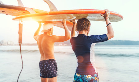 Teen boy with his father with surfboards on the heads walking in the waves on Udawalawe beach in Sri Lanka. Family active vacation or active sporty people concept.の写真素材