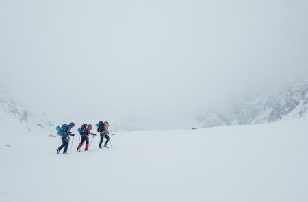 Three members rope team ascending the high mountain winter peak. Blizard covering the structural...