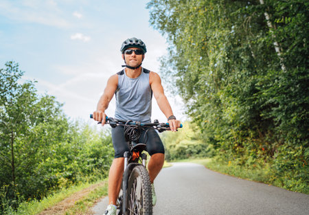 Portrait of happy man dressed in cycling clothes, helmet and sunglasses riding a bicycle on the out-of-town bicycle path. Active sporty people concept image.の写真素材