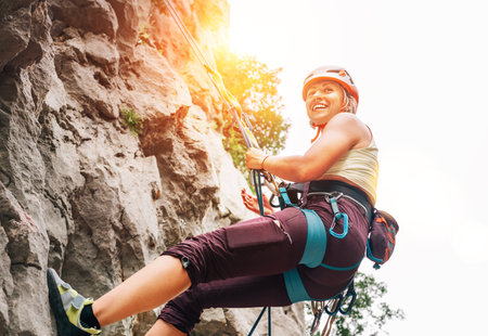 Smiling athletic woman in protective helmet and shoes climbing cliff rock wall using top rope and harness in Paklenica National park site in Croatia. Active extreme sports time spending conceptの写真素材
