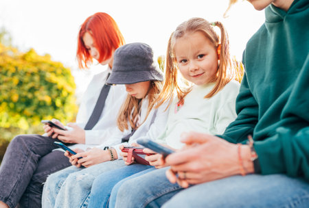 Little pretty girl portrait with sisters girls kids sitting in a row and browsing their smartphone devices. Careless young teenhood time and a modern technology concept image.の写真素材