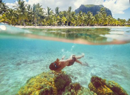 Diving teenage boy snorkeling over the coral reefs underwater photo in the clean turquoise lagoon on Le Morne palm trees beach with Le Morne Brabant mount. Mauritius island. Exotic traveling concept.の写真素材
