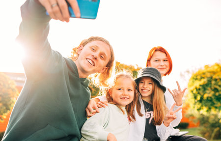 Portraits of three smiling sisters and brother teen taking selfie portrait using a modern smartphone camera. Careless young teenhood and childhood time and modern technology concept image.の写真素材