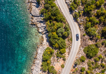 Aerial vertical shot of pickup truck moving by the curved road near sea tranquil waves on coast on Cephalonia Greek island. Transportation, traveling and nature concept.の写真素材