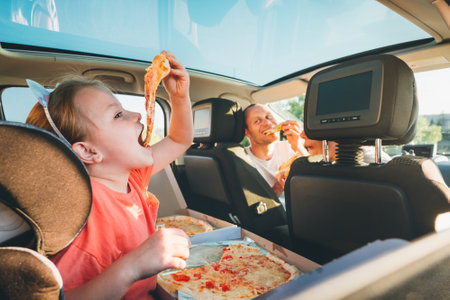 Little girl with open mouth portrait eating Italian pizza sitting in modern car with mother and father. Happy family moments, childhood, fast food eating or auto journey lunch break concept image.の写真素材