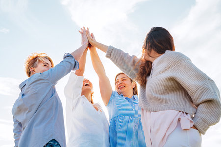 Portrait of four cheerful laughing women holding hands Up making High Five during outdoor walking. They looking at the camera. Woman's friendship, natural diversre beauty, relations, happiness imageの写真素材