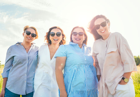 Portrait of four cheerful smiling women in sunglasses embracing and looking at the camera during outdoor walking. Woman's friendship, relations, and happiness concept image.の写真素材