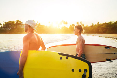 Young teen boy with a surfboard with his father go to the sea for surfing. They are smiling and enjoying a beautiful sunset light. Family active vacation concept.の写真素材