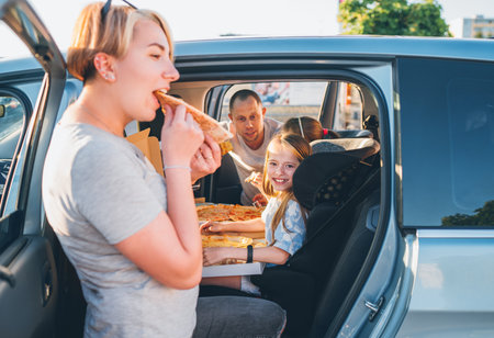 Positive smiling girl in child car seat while family car trip brake stop eating just cooked Italian pizza. Happy family moments, childhood, fast food eating or auto journey lunch break concept image.の写真素材