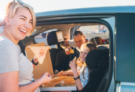 Positive smiling woman with slice of just cooked Italian pizza while family car trip stop. Happy family moments, childhood, fast food eating, family values or auto journey lunch break concept image.の写真素材