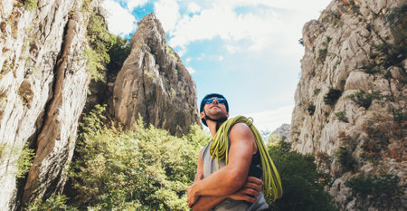 Portrait of smiling climber man in protective helmet and sunglasses with climbing rope on the shoulder standing in Paklenica park between rock cliff walls. Active extreme sports time spending concept.の写真素材