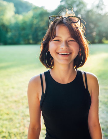 A beautiful young teenage girl cheerfully smiling at the camera with a warm sunset backlight bokeh. Beautiful people and a fashion concept image.の写真素材