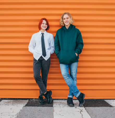Portraits of two smiling caucasian teen friends boy and girl posing for photo while they standing near the orange wall background. Careless young teenhood . time concept image.の写真素材