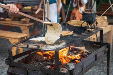Woman preparing a natural flatbread on the open fire on the metal leaf during traditional annual medieval ages restoration. Healthy food and nutrition concept image.の写真素材