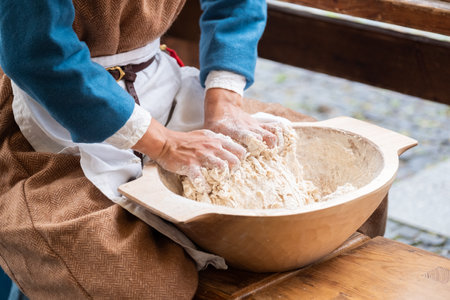 Woman dressed medieval costume sitting and kneading the fresh wheat dought. Healthy food and nutrition concept image.の写真素材