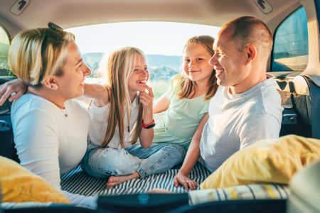 Portrait of happy smiling little sisters. Happy young couple with two daughters inside the car trunk during auto trop. They are smiling, laughing and chatting. Family values, traveling concept.の写真素材