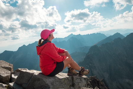 Trekker woman dressed red active people clothes sitting on Rysy peak 2499m enjoying High Tatras...