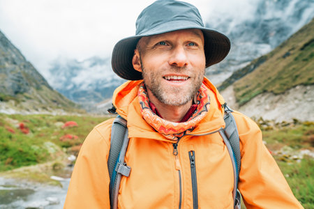 Portrait of smiling Man with backpack dressed orange waterproof jacket and funny hat walking the path during Makalu Barun National Park trek in Nepal. Mountain hiking and active people concept image.の写真素材