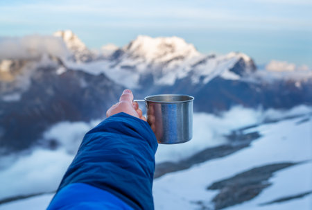 Young woman holding a metal hot tea cup during sunset time from the Mera Peak high camp with snowy seven-thousander mountains. Climbing expedition acclimatization. Active people concept.の写真素材