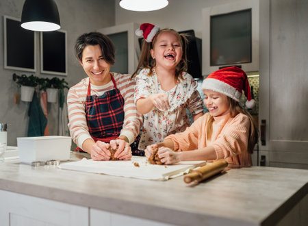 Laughing little girls in red Santa hat with mother kneading Christmas gingerbread dough together in home kitchen. Happy holidays preparation and childhood concept.の写真素材