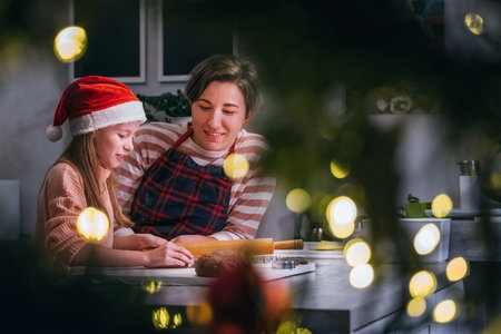 Cute little girl in red Santa hat with mother making homemade Christmas gingerbread cookies using rolling pin together in home kitchen. Happy family holidays preparation and childhood concept..の写真素材