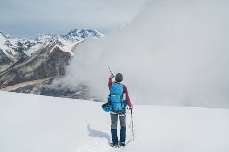 Climber with backpack and trekking poles descending Mera peak high slopes at cca 6000m and pointing at legendary Mount Everest, Nuptse, Lhotse with South Face wall, Makalu beautiful High Himalayas.の写真素材