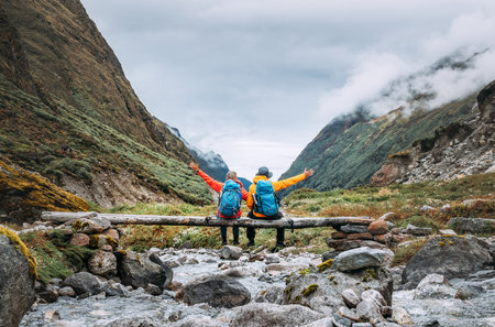 Trekkers Couple sitting on wooden bridge on Mera Peak trekking route near Kothe. Man and woman joyfully raising arms UP. They enjoying  Makalu Barun National Park valley view.の写真素材