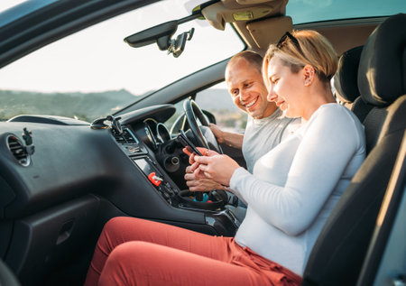 Happy smiling two young adulds couple using smartphone navigation inside car during auto jorney.They are laughing during road trip. Family, couples relations values, car sharing and traveling conceptsの写真素材