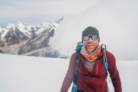 Cheerful laughing climber in sunglasses portrait with backpack ascending Mera peak high slopes at...
