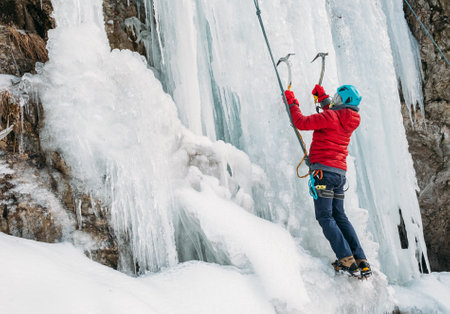 Ice climber dressed in warm winter climbing clothes, safety harness and helmet climbing frozen waterfall using two Ice climbing axes and crampons. Active people and sports activities concept image.の写真素材