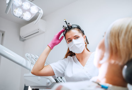 Dental clinic patient appointment in modern medical ward. Dentist doctor in magnifying glasses smiling with eyes young Female ready for teeth surgery. Health care and medicare industry concept imageの写真素材