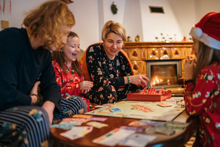 Mother, son and daughters kids playing together table board game, wearing Christmas hats. Cozy pre Christmas evening time moment near fireplace. Family values, board games, X-mas celebration concept.の写真素材