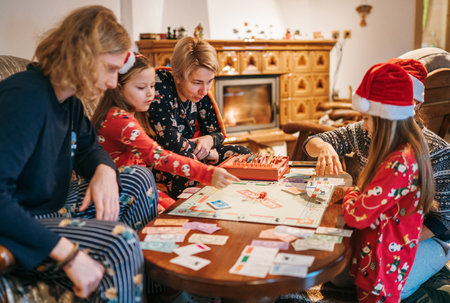 Mother with son and daughters kids playing together table board game, wearing Christmas hats. Cozy pre Christmas evening time moment. Family values, board games and X-mas celebration concept.の写真素材